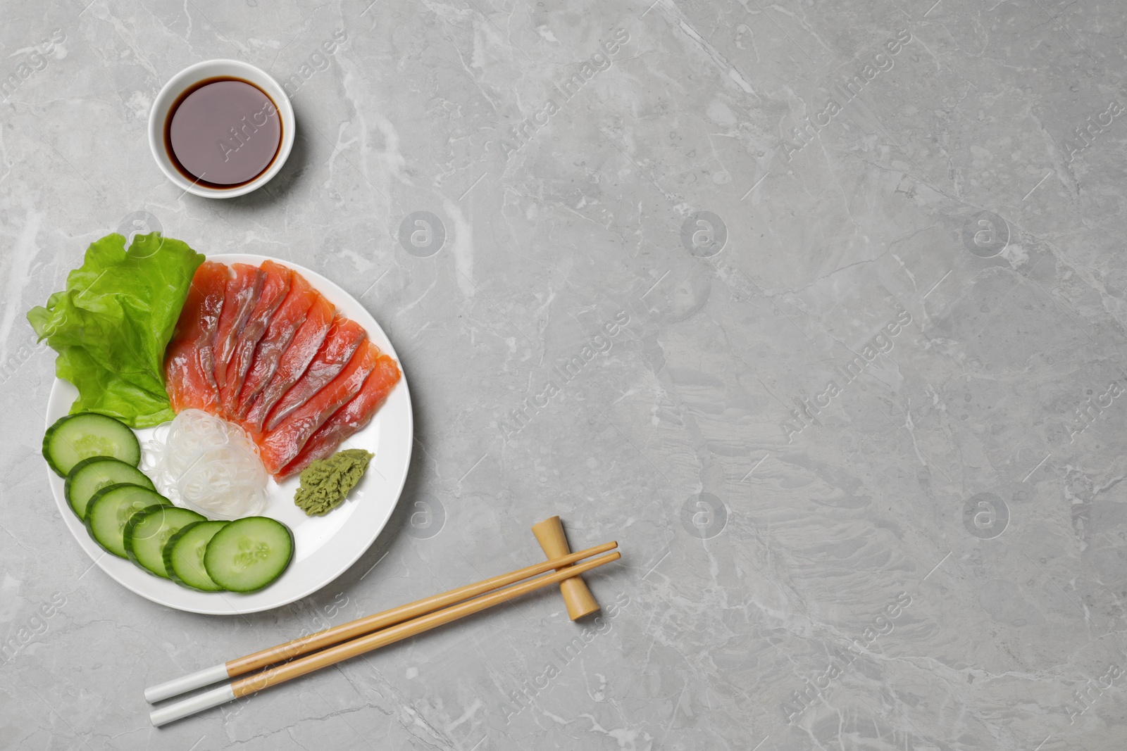 Photo of Sashimi set (salmon slices) with cucumber, greens, vasabi and funchosa served with soy sauce on light grey table, flat lay. Space for text