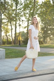 Photo of Beautiful young woman in stylish white dress with handbag outdoors