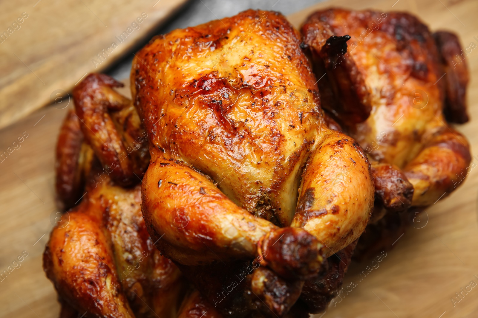 Photo of Delicious grilled whole chickens on wooden board, closeup