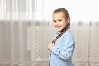 Photo of Cute little girl with braided hair indoors. Space for text