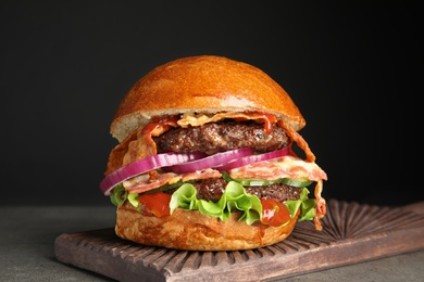 Tasty burger with bacon on table against black background