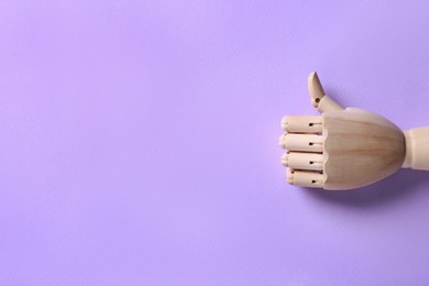 Photo of Wooden mannequin hand showing thumb up on lilac background, top view. Space for text