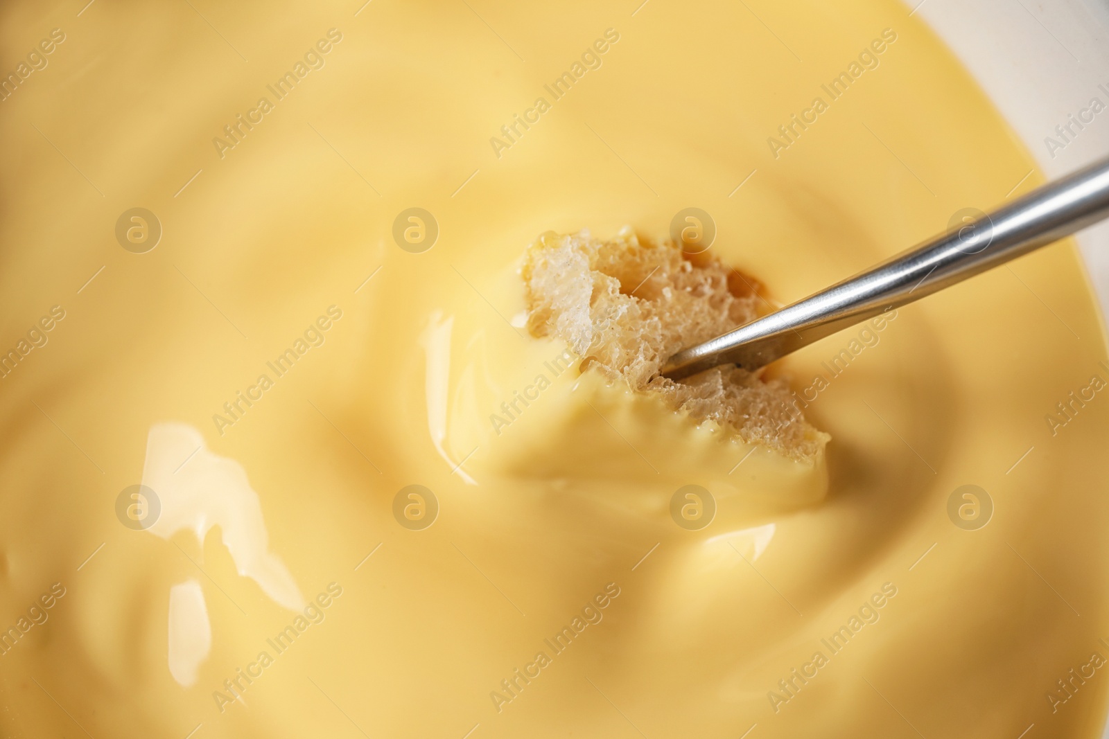 Photo of Dipping bread into tasty cheese fondue, closeup