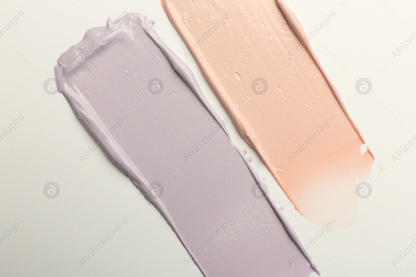 Photo of Strokes of pink and purple color correcting concealers on white background, top view