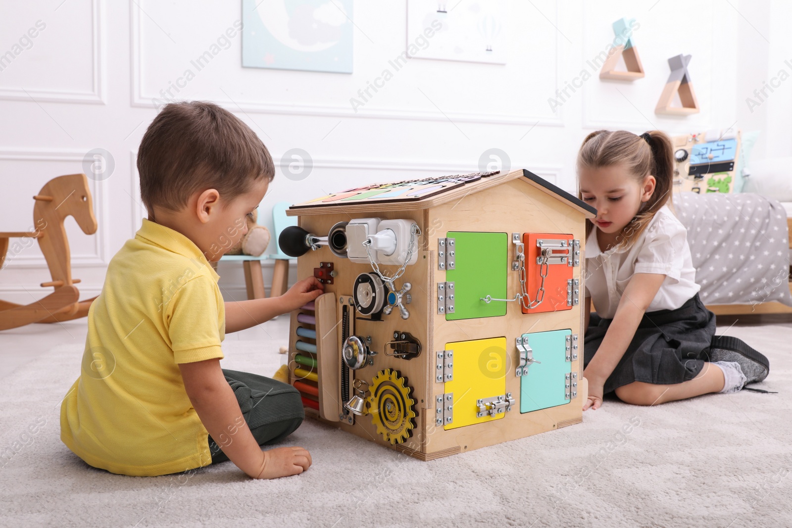 Photo of Little boy and girl playing with busy board house on floor in room