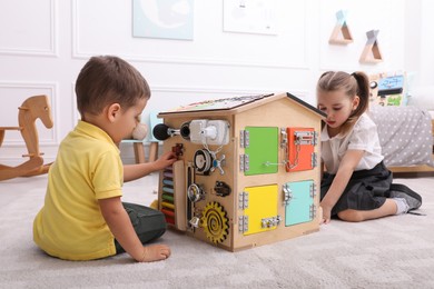 Photo of Little boy and girl playing with busy board house on floor in room