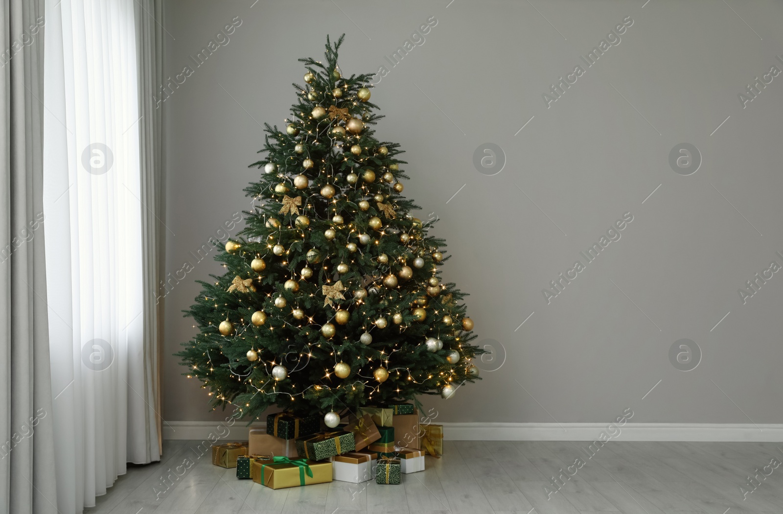 Photo of Beautifully decorated Christmas tree and gifts near grey wall indoors, space for text