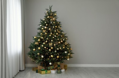 Photo of Beautifully decorated Christmas tree and gifts near grey wall indoors, space for text