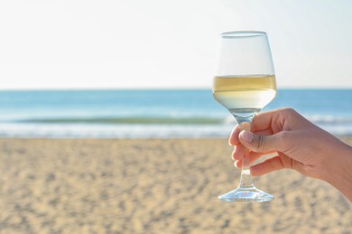 Photo of Woman with glass of tasty wine near sea, closeup. Space for text