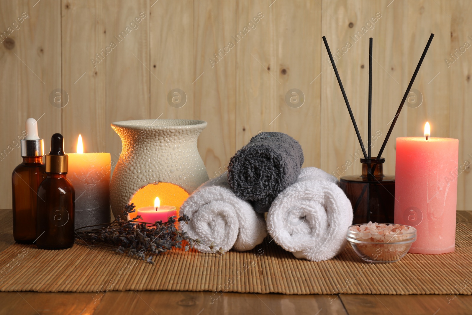 Photo of Aromatherapy. Scented candles, bottles, lavender, towels and sea salt on wooden table