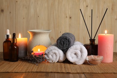 Aromatherapy. Scented candles, bottles, lavender, towels and sea salt on wooden table