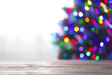 Photo of Blurred view of beautiful Christmas tree with colorful lights near window indoors, focus on wooden table. Space for text