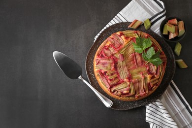 Photo of Freshly baked rhubarb pie, cut stalks and cake server on black table, flat lay. Space for text