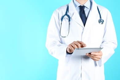 Photo of Male doctor holding modern tablet on color background, closeup with space for text