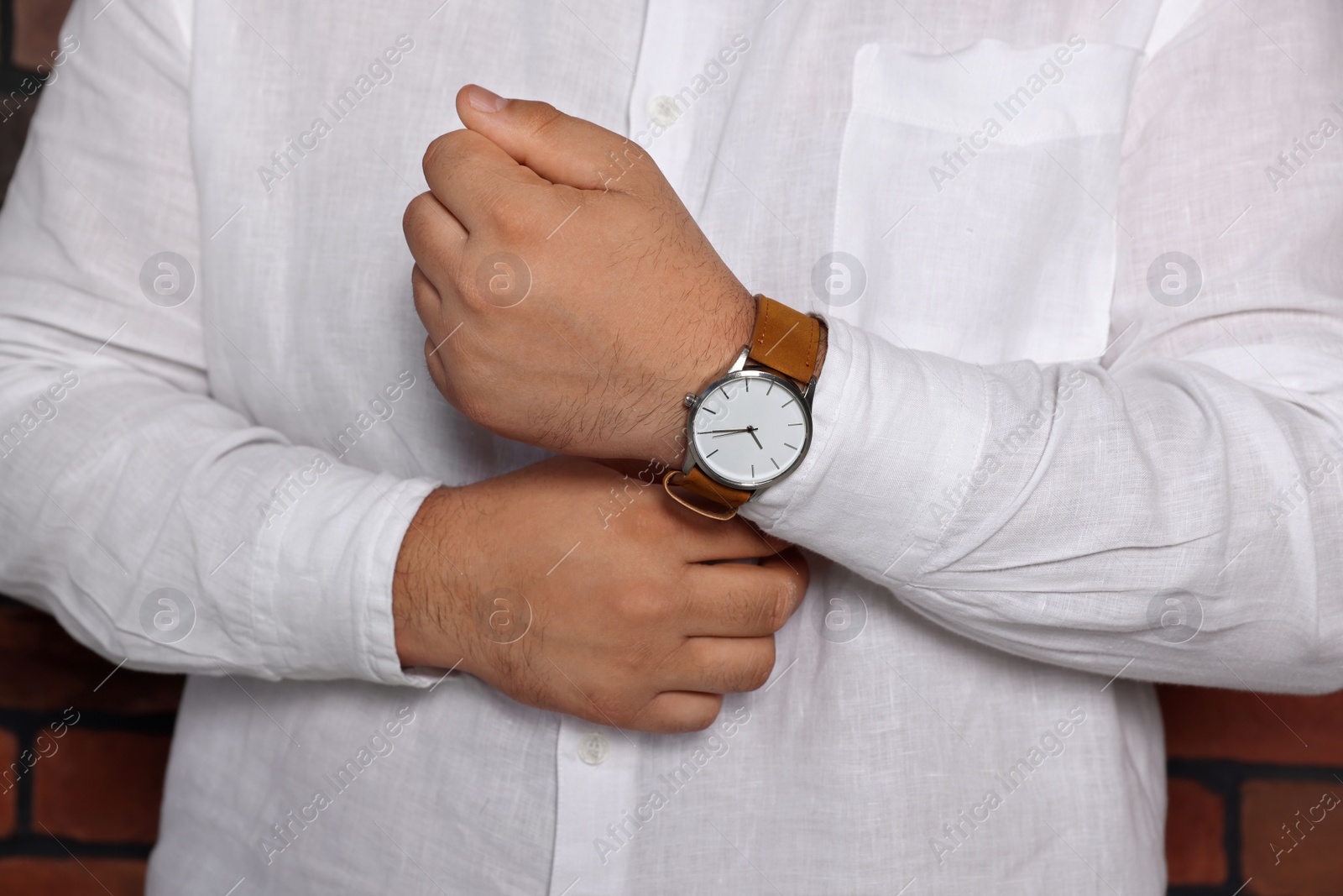 Photo of Groom adjusting watch near red brick wall, closeup. Wedding day