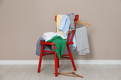 Photo of Different clothes on red chair and hangers near light grey wall