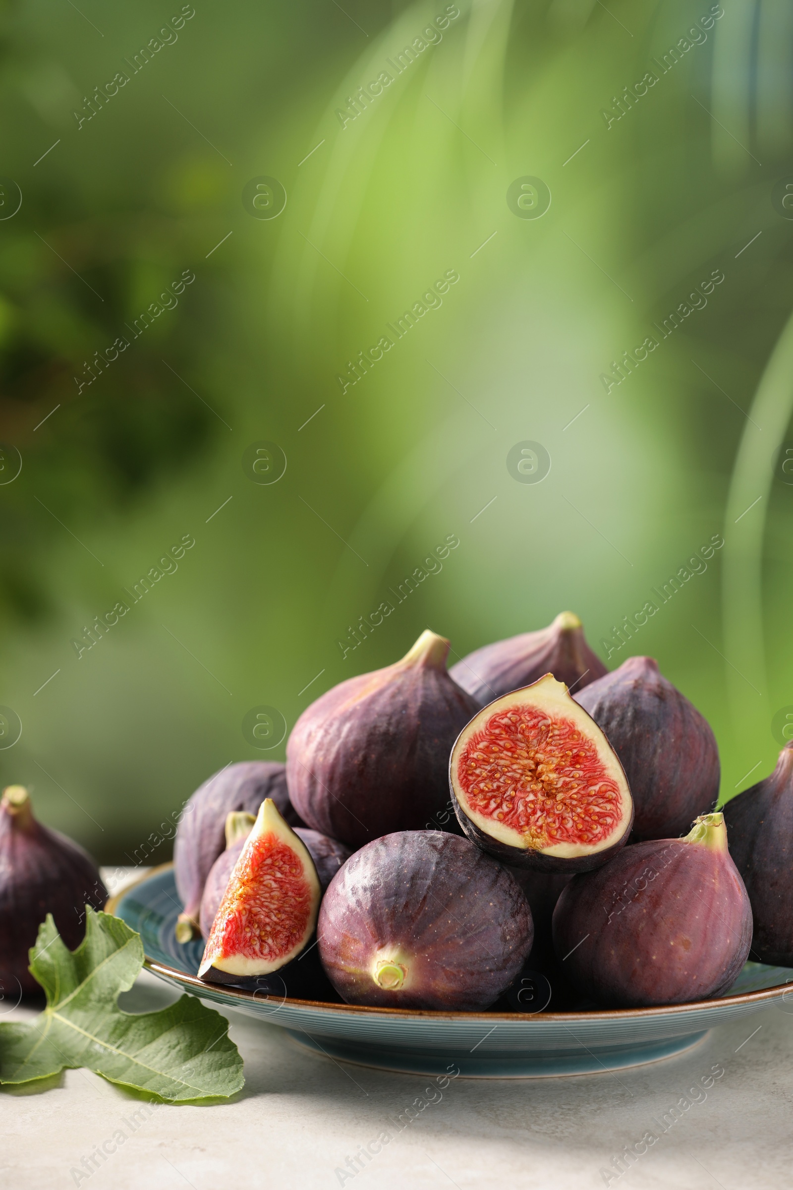 Photo of Plate with fresh ripe figs and green leaf on light table. Space for text