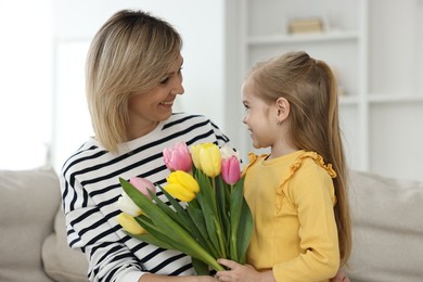 Little daughter congratulating her mom with bouquet of beautiful tulips at home. Happy Mother's Day