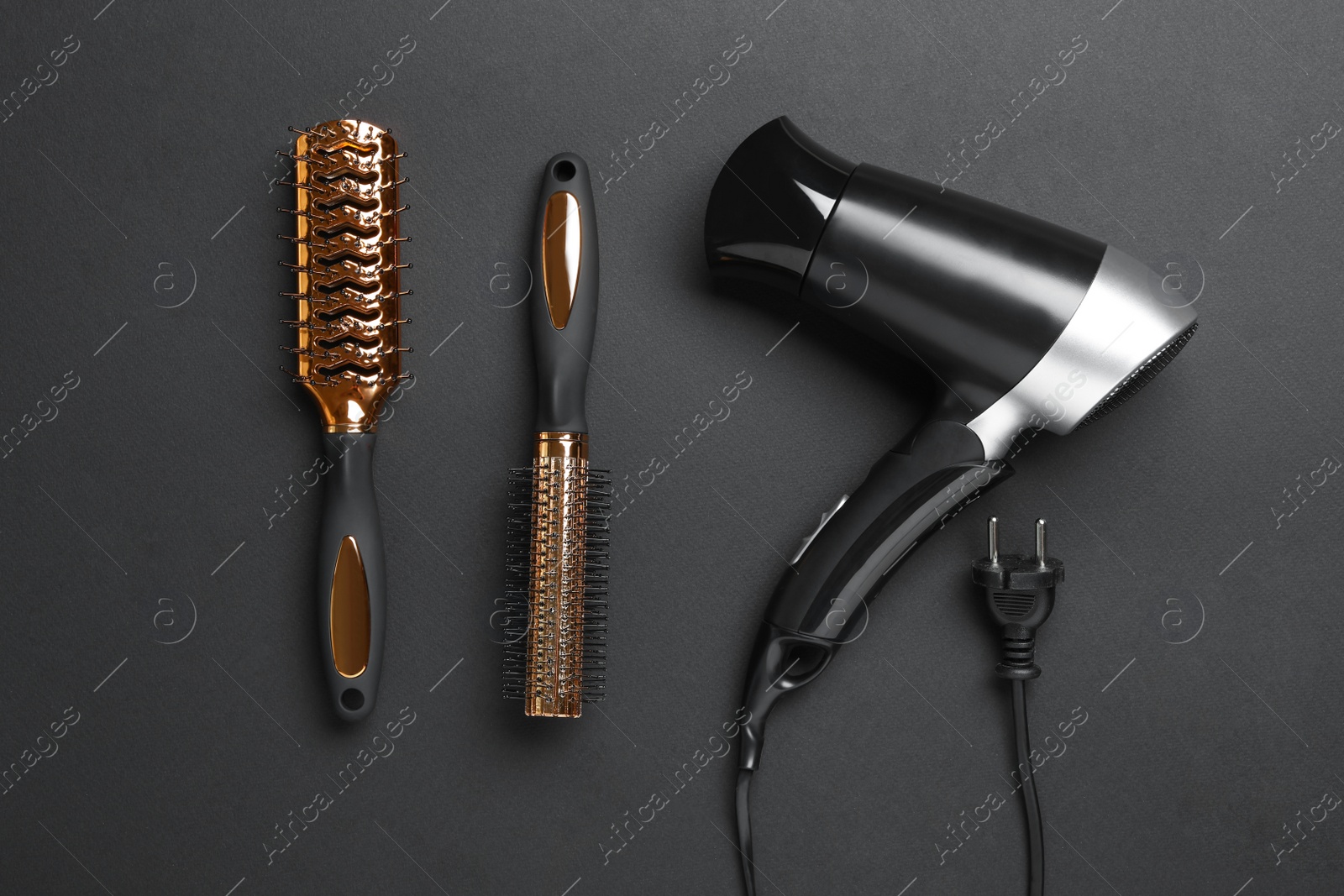 Photo of Hair dryer and brushes on black background, flat lay. Professional hairdresser tool
