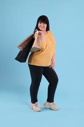 Beautiful overweight mature woman with shopping bags on turquoise background