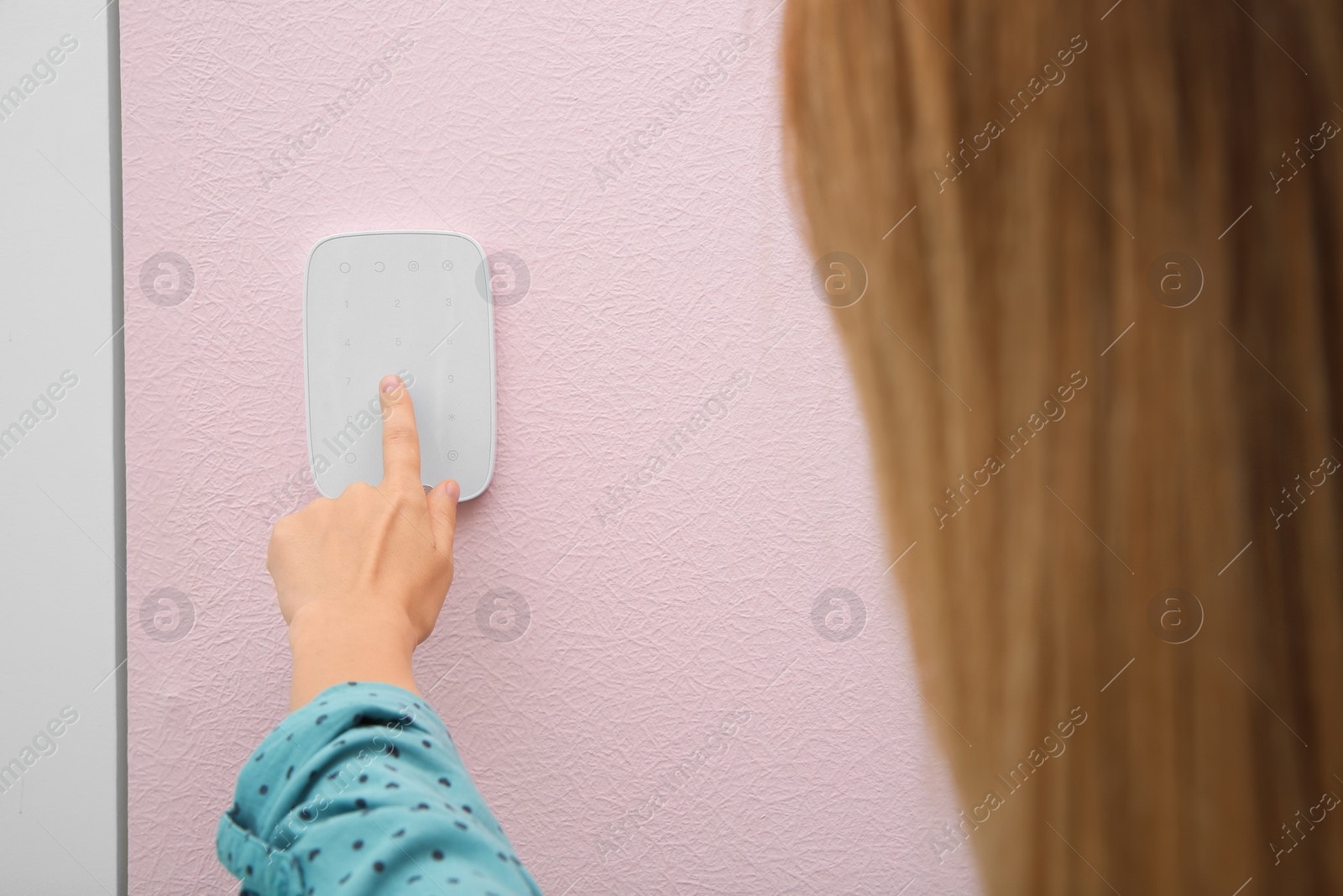 Photo of Young woman entering code on alarm system keypad indoors
