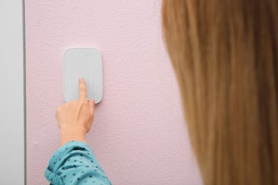 Young woman entering code on alarm system keypad indoors