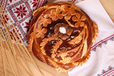 Photo of Rushnyk with korovai, wheat spikes on wooden table, flat lay. Ukrainian bread and salt welcoming tradition