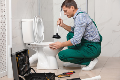 Professional plumber unclogging drain of toilet bowl in bathroom