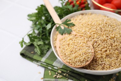 Photo of Bowl and spoon with raw bulgur on table, closeup