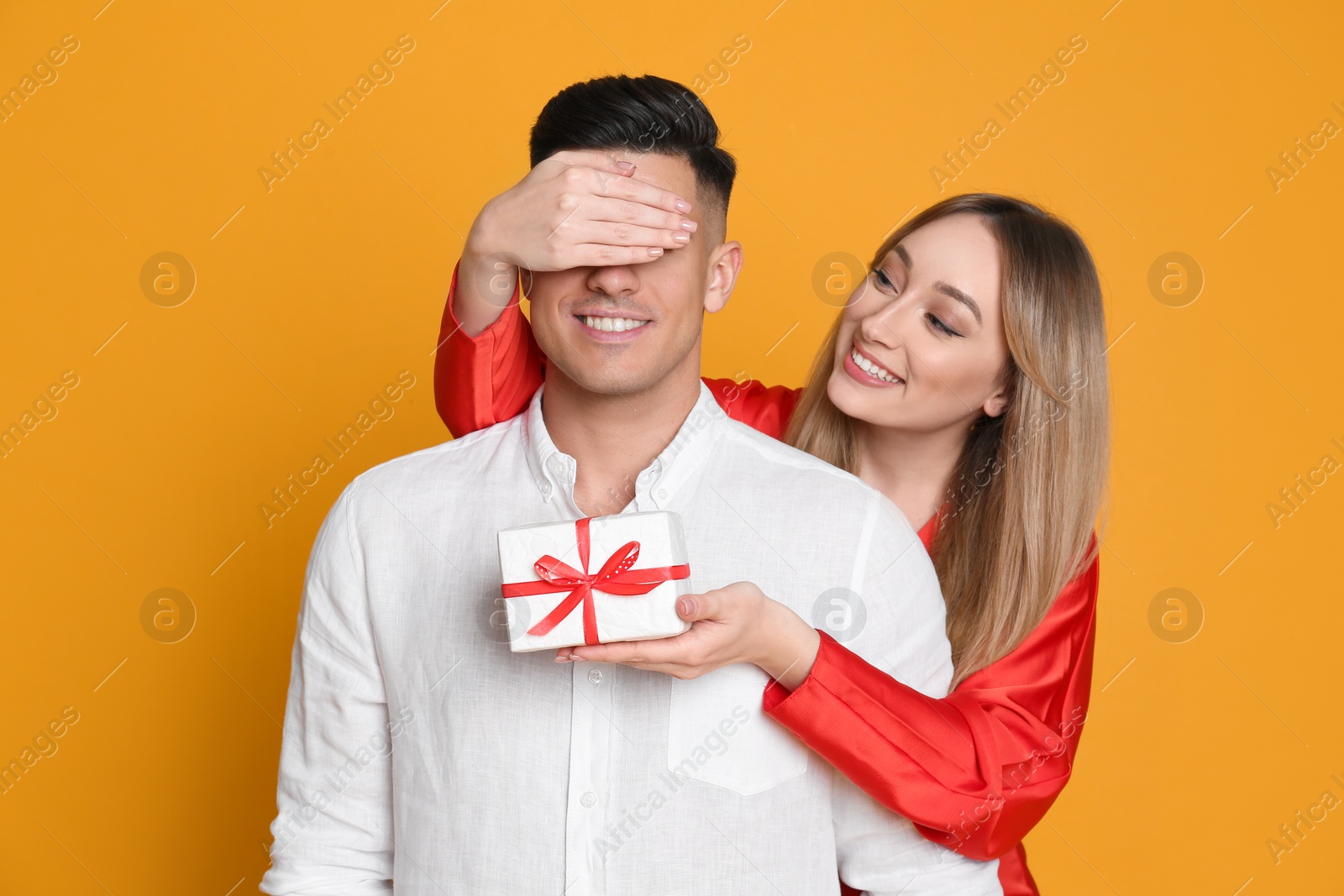 Photo of Woman surprising her boyfriend with gift on yellow background. Valentine's day celebration