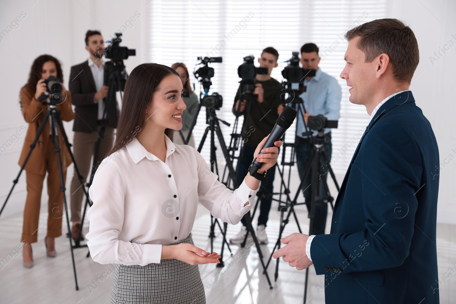 Photo of Professional young journalist interviewing businessman and group of video camera operators on background