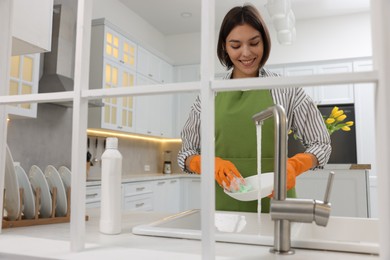 Photo of Happy young woman washing plate above sink in modern kitchen