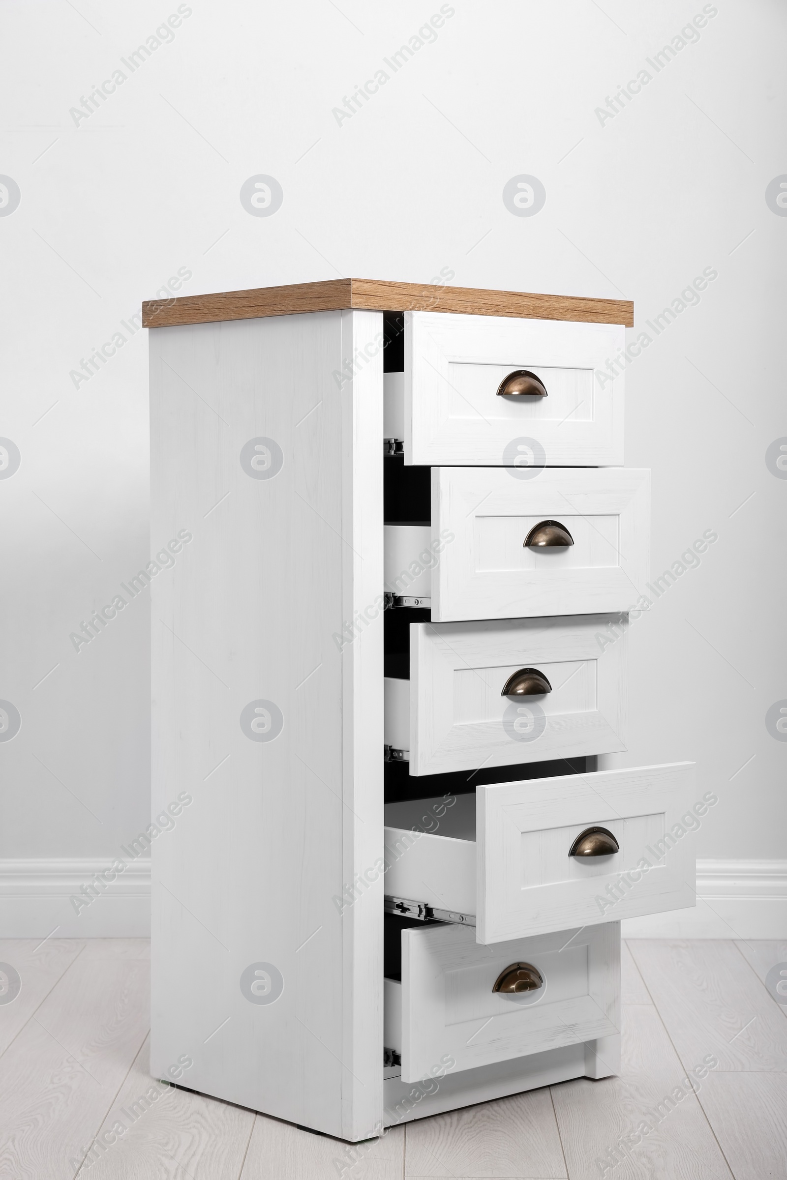 Photo of Stylish chest of drawers near white wall. Furniture for wardrobe room