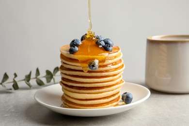 Photo of Pouring honey onto tasty pancakes with berries on table