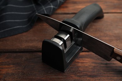 Photo of Modern handheld sharpener and knife on wooden table