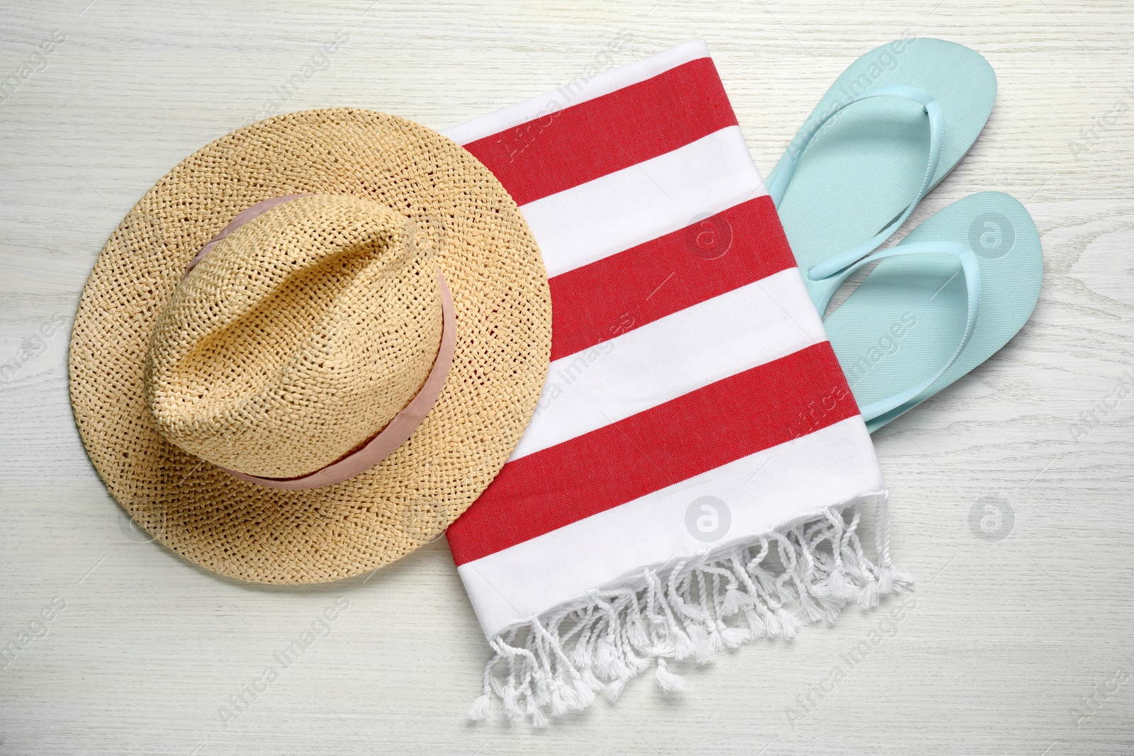 Photo of Beach towel, flip flops and straw hat on white wooden background, flat lay