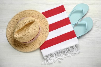 Beach towel, flip flops and straw hat on white wooden background, flat lay