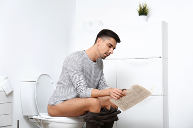 Photo of Man with newspaper sitting on toilet bowl in bathroom