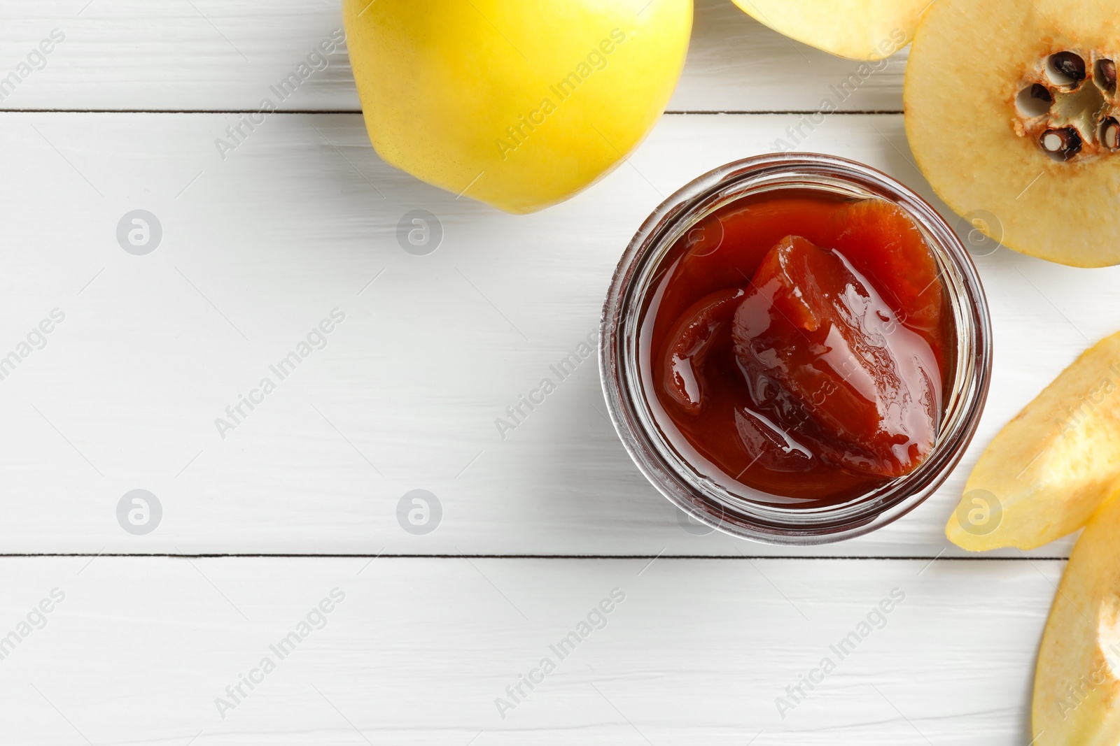 Photo of Tasty homemade quince jam in jar and fruits on white wooden table, flat lay. Space for text
