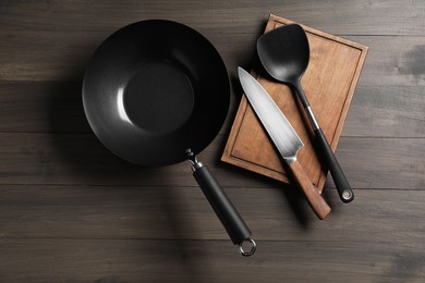 Black metal wok, knife, board and spatula on wooden table, top view