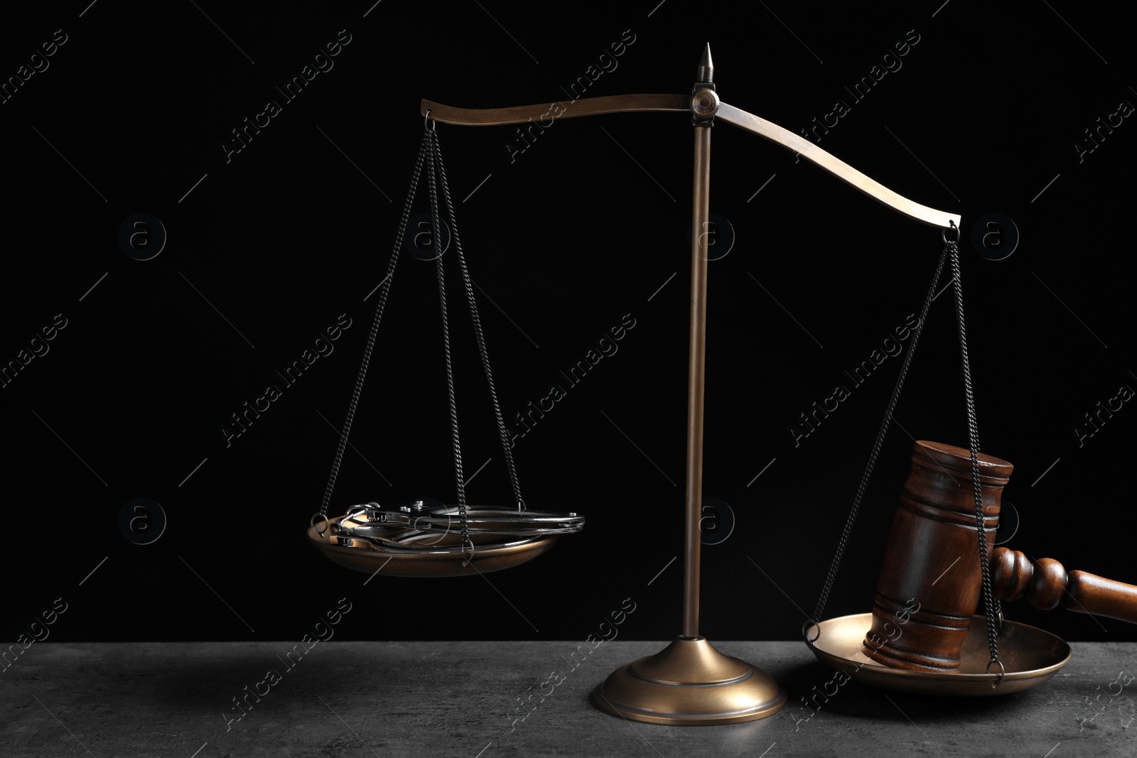 Photo of Judge's gavel and scales on grey table against black background. Criminal law concept