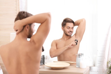 Photo of Handsome young man applying deodorant in bathroom