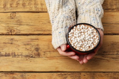 Photo of Woman with cup of tasty hot chocolate and marshmallows at wooden table, top view. Space for text