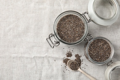 Photo of Glass jars and spoon with chia seeds on fabric, flat lay. Space for text