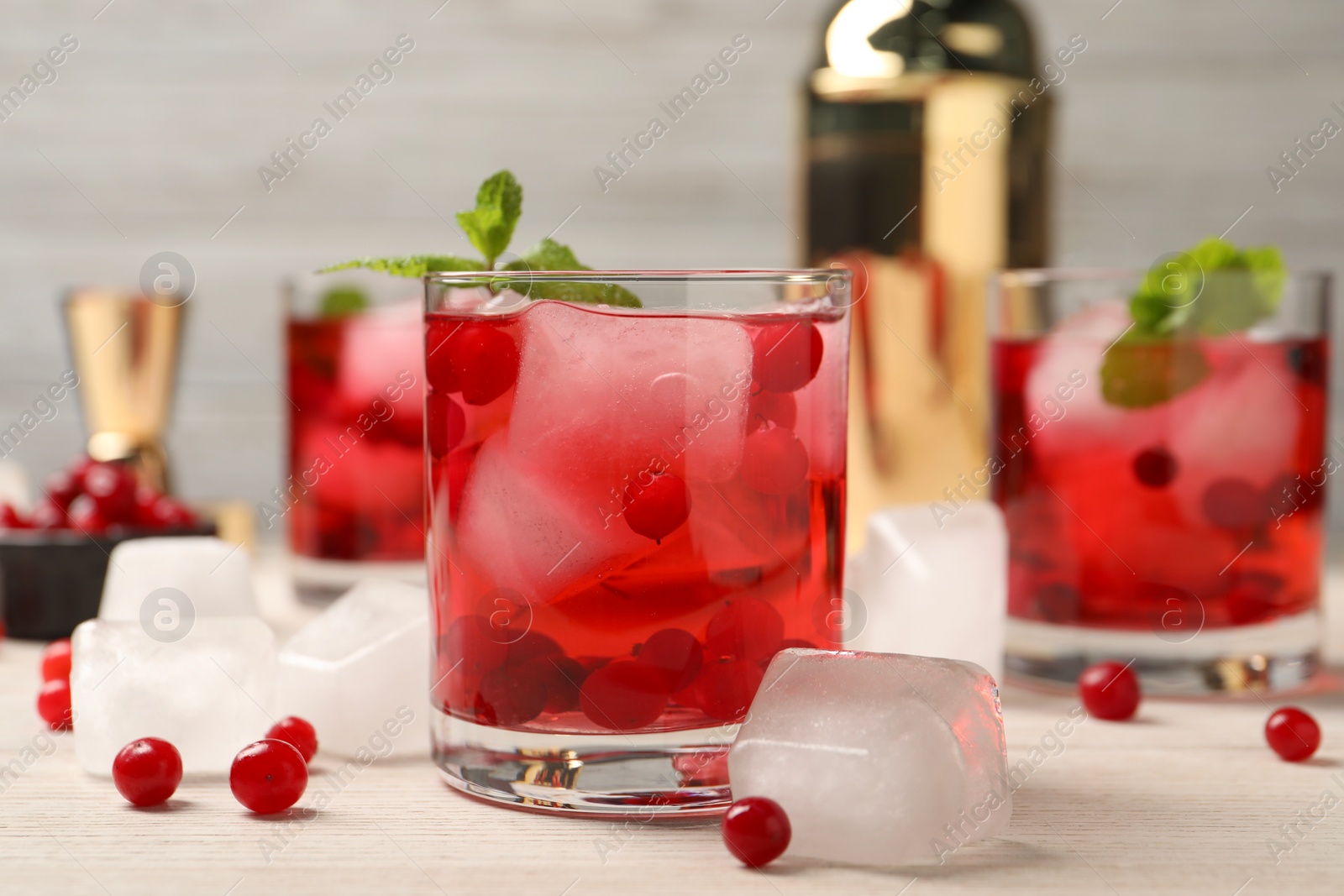 Photo of Tasty cranberry cocktail with ice cubes in glasses and fresh berries on wooden table