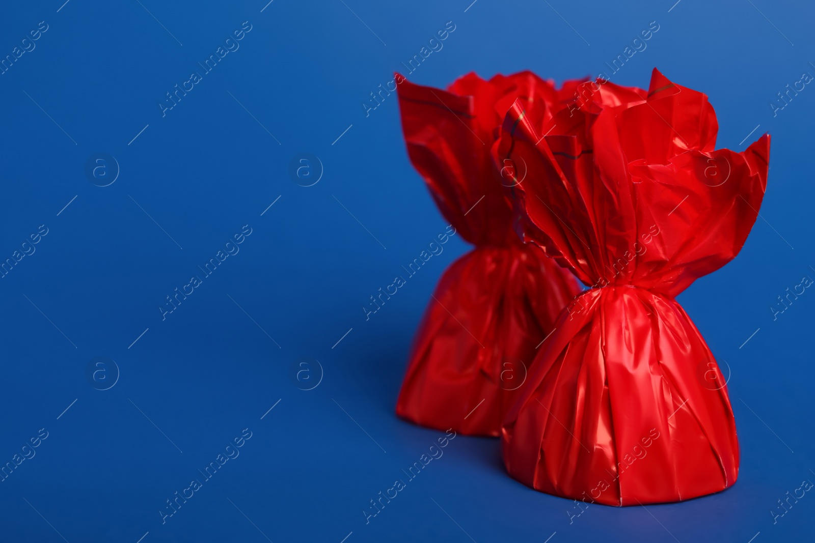 Photo of Candies in red wrappers on blue background. Space for text