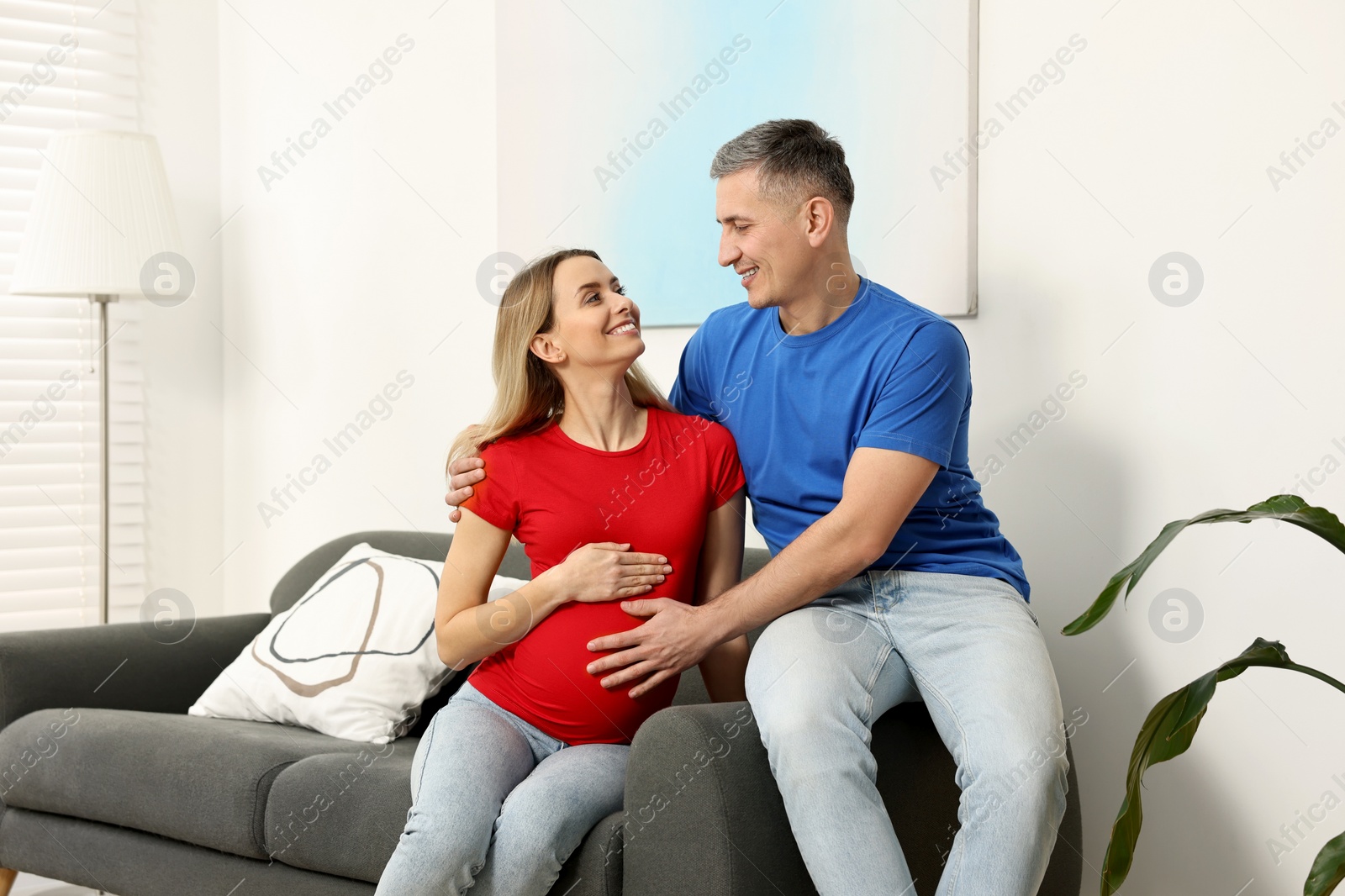 Photo of Young family housing concept. Pregnant woman with her husband on sofa at home