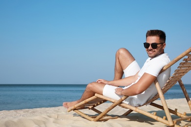 Photo of Young man relaxing in deck chair on sandy beach