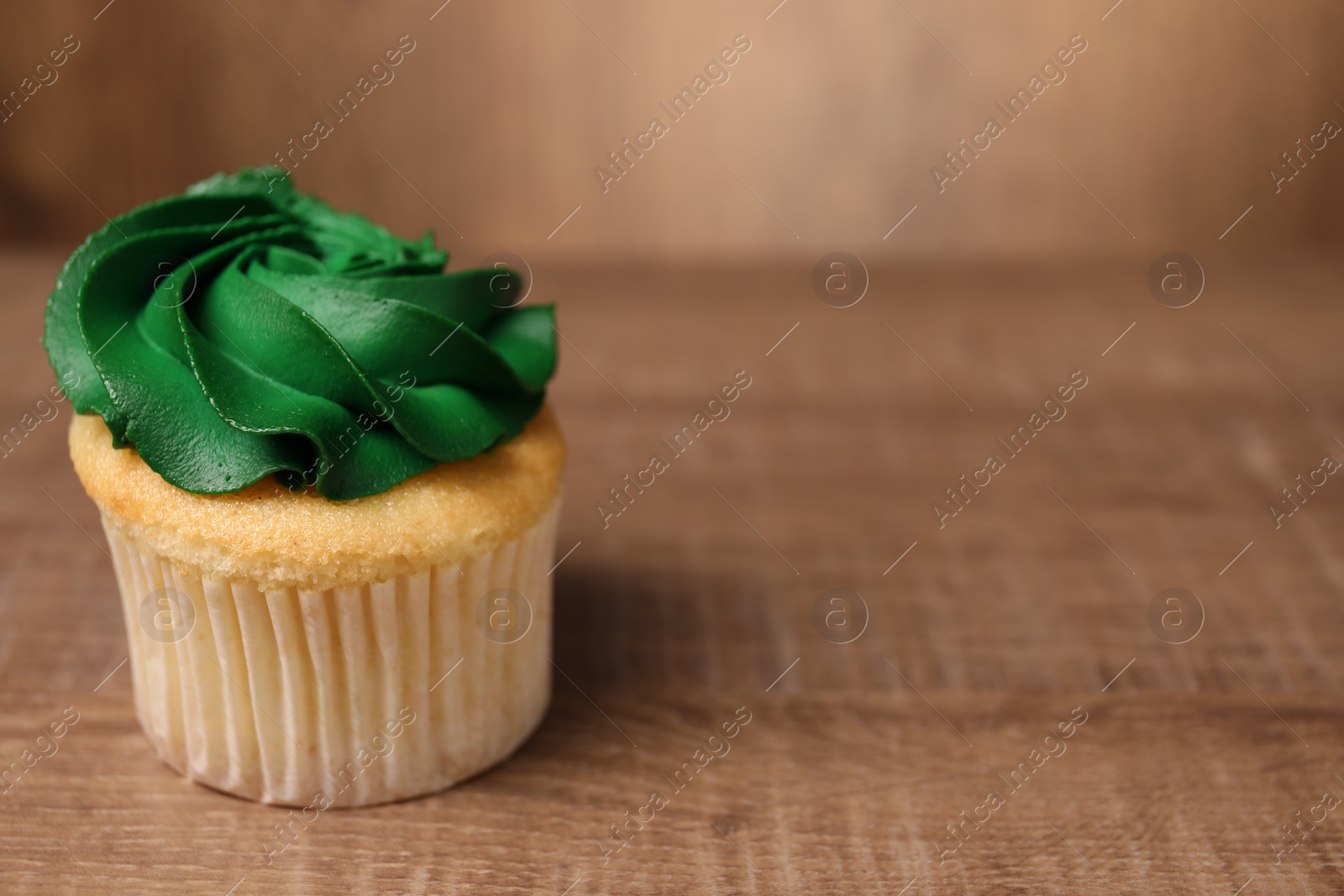 Photo of Delicious cupcake with bright cream on wooden table, closeup. Space for text