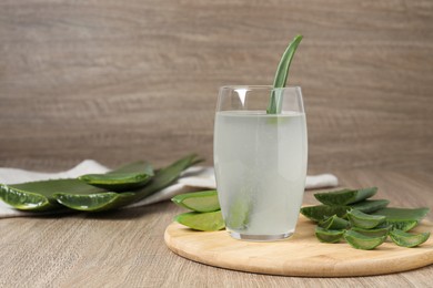 Photo of Tasty aloe juice in glass and cut fresh leaves on wooden table